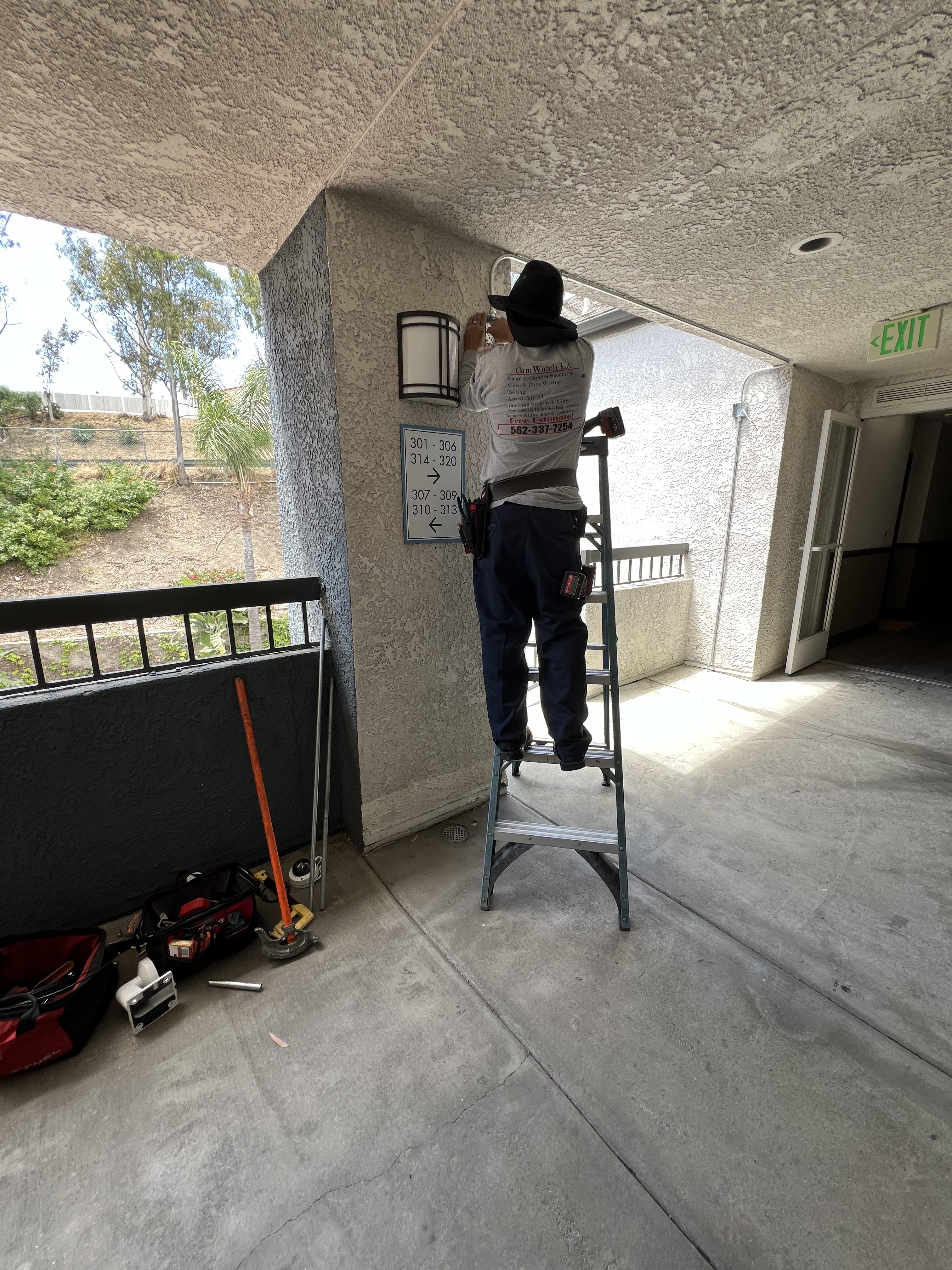 A technician installing a security camera on a wall while standing on a ladder in a property located at San Pedro, CA