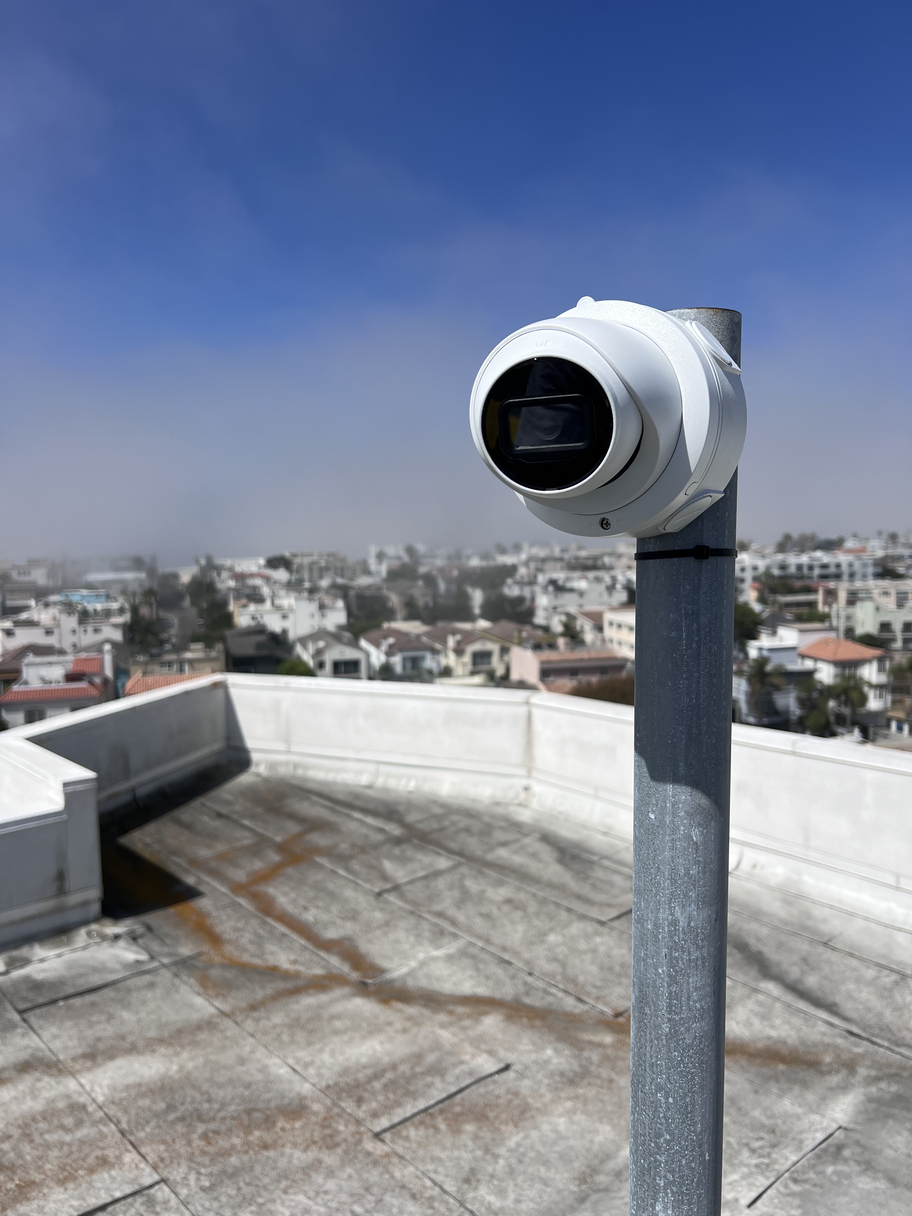 Close-up of a security camera mounted on a pole, overlooking roof in Marina Del Rey, CA under a clear blue sky in Los Angeles, CA